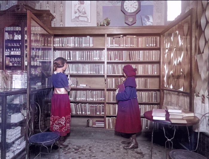An old photo of two people looking through a large collection of books