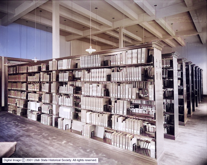 Rows of bookshelves filled with books and documents in a large, well-lit library room.